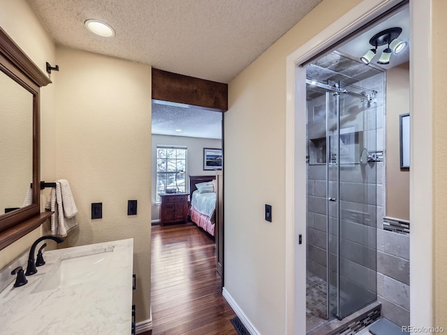 ensuite bathroom with a textured ceiling, a shower stall, wood finished floors, and vanity