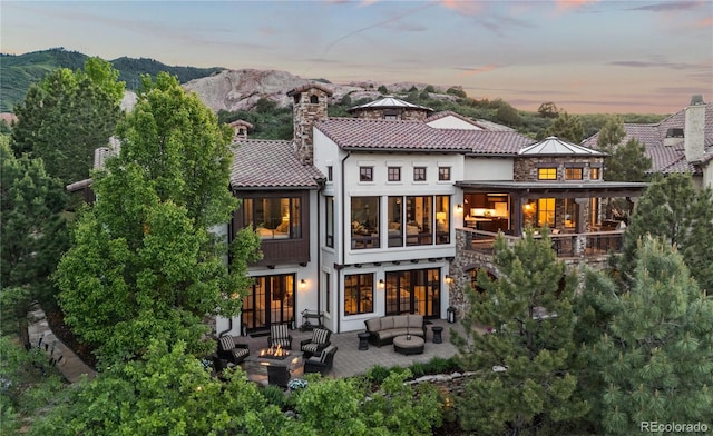 7208 Raphael Ln, Littleton, CO 80125 - back of property at dusk featuring an outdoor living space with a fire pit, a mountain view, a balcony, a patio, and stucco siding