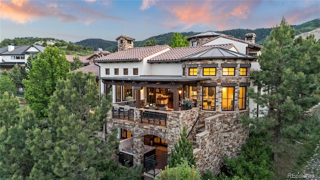 7208 Raphael Ln, Littleton, CO 80125 - rear view of house with stone siding, a balcony, a mountain view, and a chimney