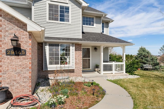 doorway to property with covered porch, a shingled roof, and a yard