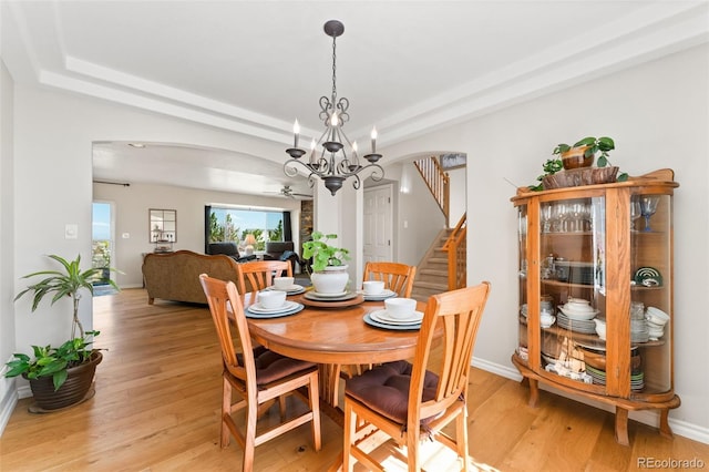 dining area with arched walkways, ceiling fan, light wood-style flooring, a chandelier, and stairs
