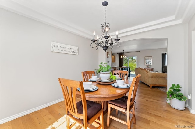 dining space featuring a chandelier, light wood finished floors, baseboards, and arched walkways