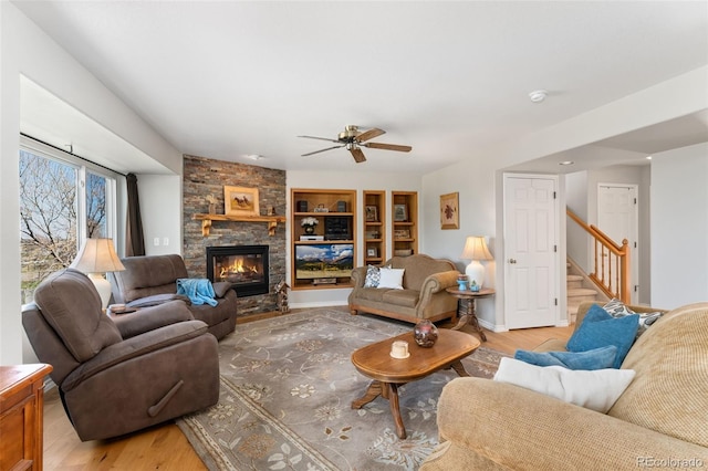 living room featuring light wood finished floors, ceiling fan, stairs, and a fireplace