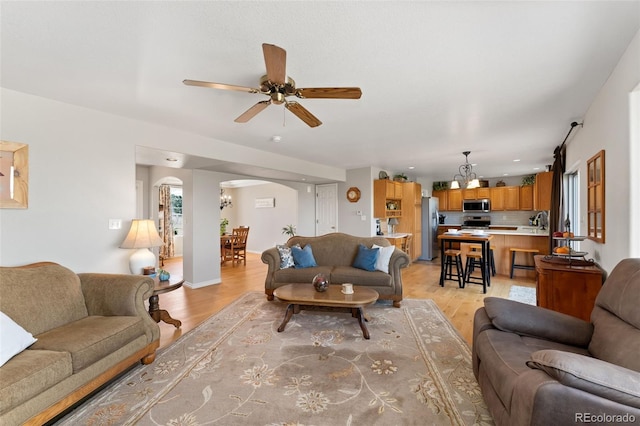 living area with arched walkways, light wood-type flooring, and ceiling fan