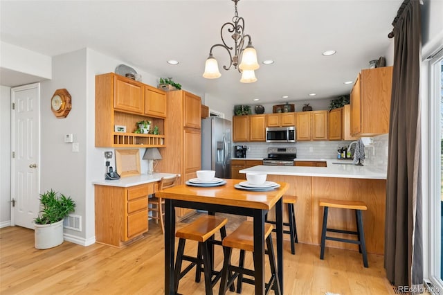 kitchen with appliances with stainless steel finishes, backsplash, light wood finished floors, light countertops, and recessed lighting