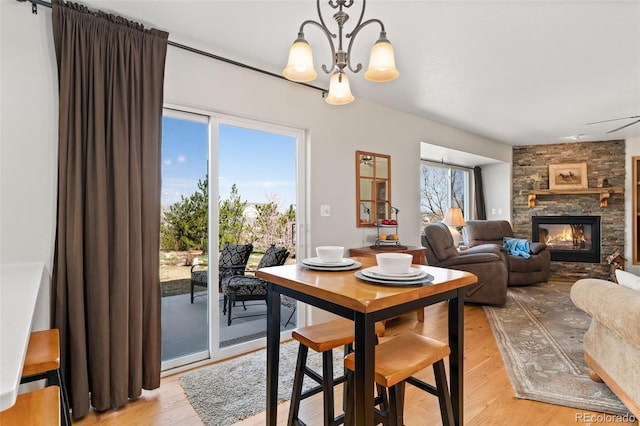 dining room featuring light wood finished floors, a chandelier, and a stone fireplace