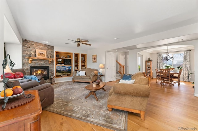 living room with a fireplace, stairway, ceiling fan, arched walkways, and light wood-style flooring