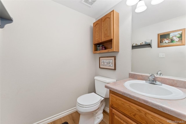 half bath with wood finished floors, toilet, vanity, and baseboards