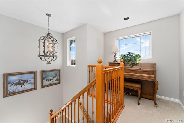 corridor with an upstairs landing, a chandelier, healthy amount of natural light, and light carpet