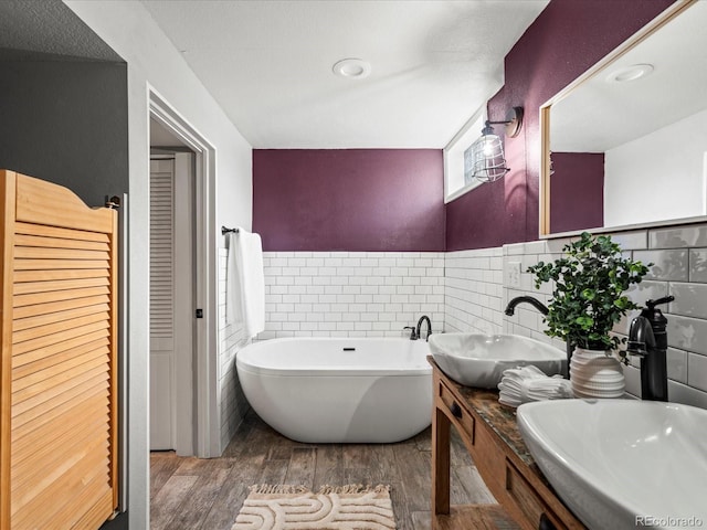 bathroom with a tub to relax in, vanity, hardwood / wood-style flooring, and tile walls