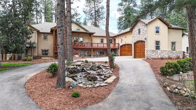 view of front of home with stone siding, curved driveway, stucco siding, a gate, and an attached garage