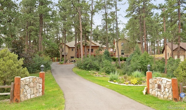 view of property's community with asphalt driveway, view of wooded area, and a yard