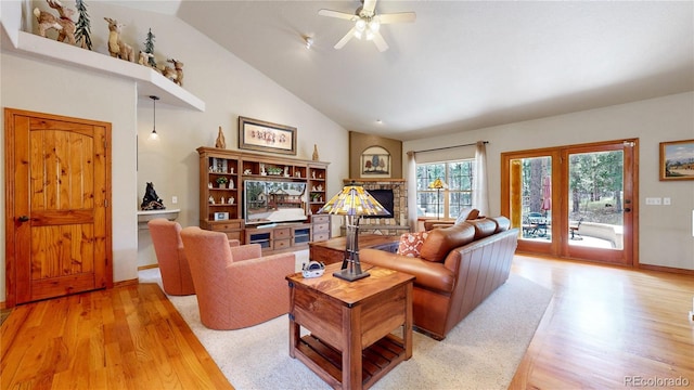 living room with light wood-type flooring, a stone fireplace, vaulted ceiling, a ceiling fan, and baseboards