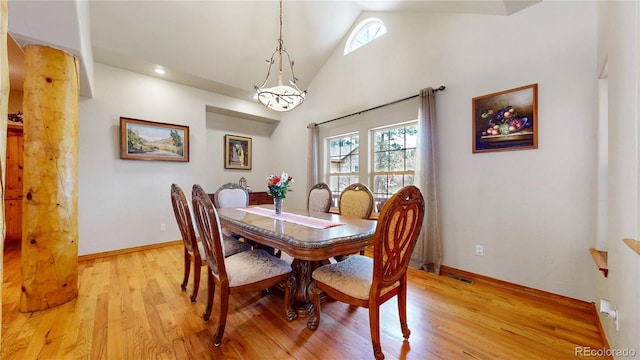 dining space with healthy amount of natural light, light wood finished floors, high vaulted ceiling, and baseboards