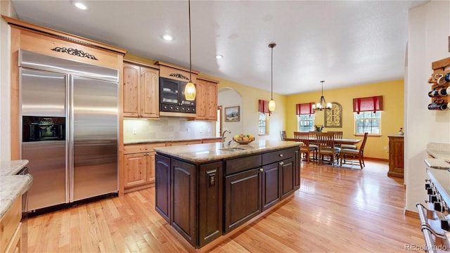 kitchen with built in fridge, light wood-type flooring, arched walkways, light stone countertops, and backsplash
