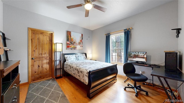 bedroom featuring wood finished floors, an office area, a ceiling fan, and baseboards