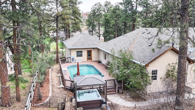 rear view of house with a hot tub, stucco siding, a fenced backyard, and roof with shingles