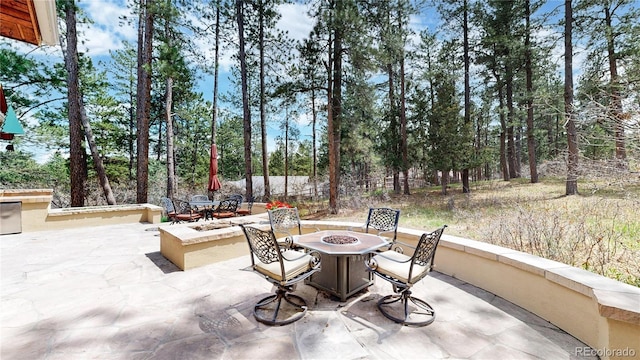view of patio with an outdoor fire pit, outdoor dining area, and view of scattered trees