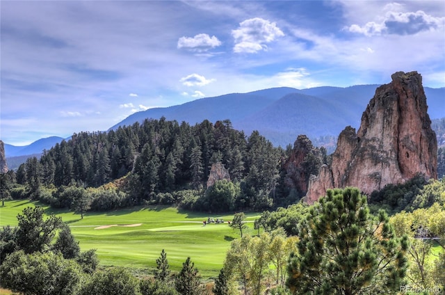 view of mountain background featuring a local golf course and a heavily wooded area