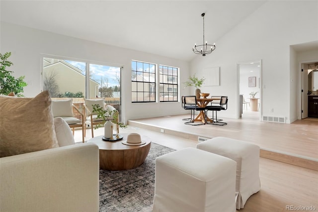 living room with high vaulted ceiling, a chandelier, and light hardwood / wood-style flooring