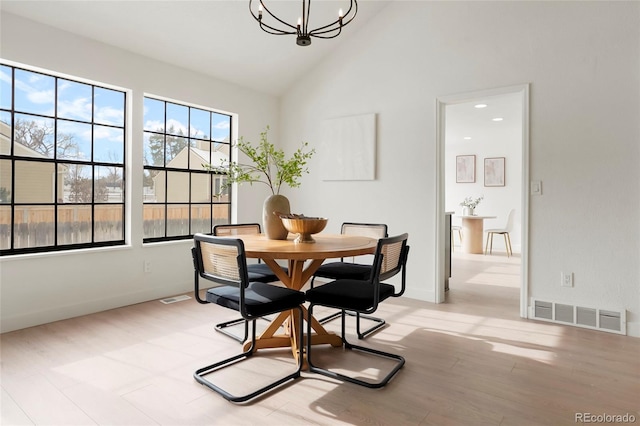 dining space featuring a notable chandelier, light hardwood / wood-style flooring, and high vaulted ceiling