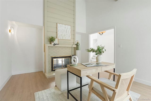 office space featuring a towering ceiling, a brick fireplace, and light wood-type flooring