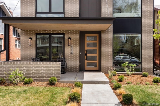 view of exterior entry with brick siding and covered porch