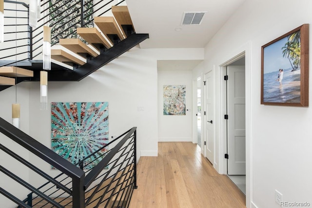 hall with light wood-style floors, baseboards, stairs, and visible vents