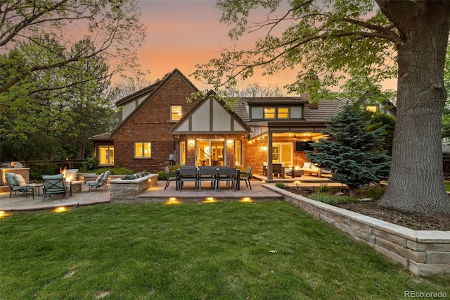 back of property at dusk featuring an outdoor living space with a fire pit, a patio, a yard, and brick siding