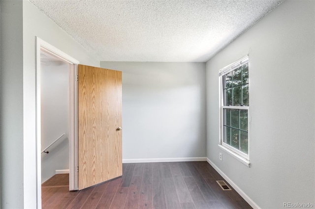 unfurnished room with a textured ceiling, dark wood finished floors, visible vents, and baseboards