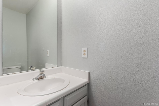 half bath featuring toilet, vanity, and a textured wall