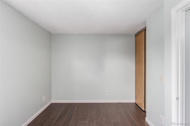 empty room featuring a textured ceiling, dark wood-style flooring, and baseboards