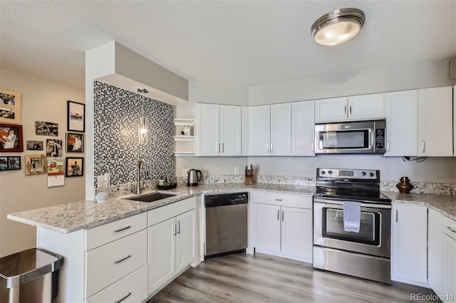 kitchen with kitchen peninsula, appliances with stainless steel finishes, light hardwood / wood-style flooring, white cabinetry, and sink