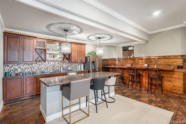 kitchen featuring crown molding, dark wood-type flooring, stainless steel appliances, a breakfast bar area, and backsplash