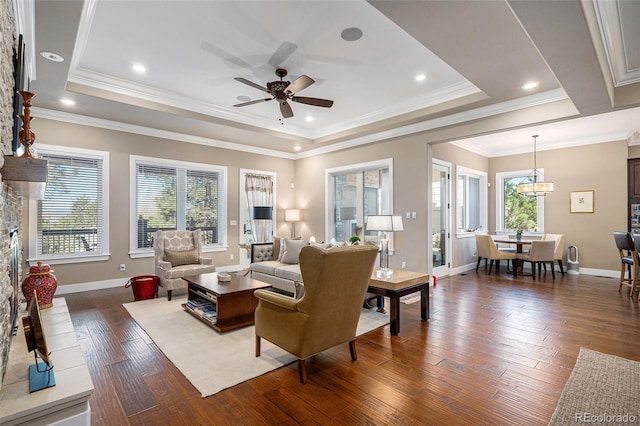 living area featuring baseboards, a ceiling fan, crown molding, a tray ceiling, and dark wood finished floors