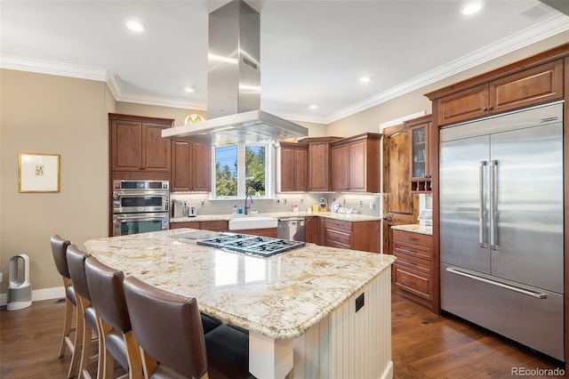 kitchen with ornamental molding, light stone counters, stainless steel appliances, brown cabinets, and island range hood