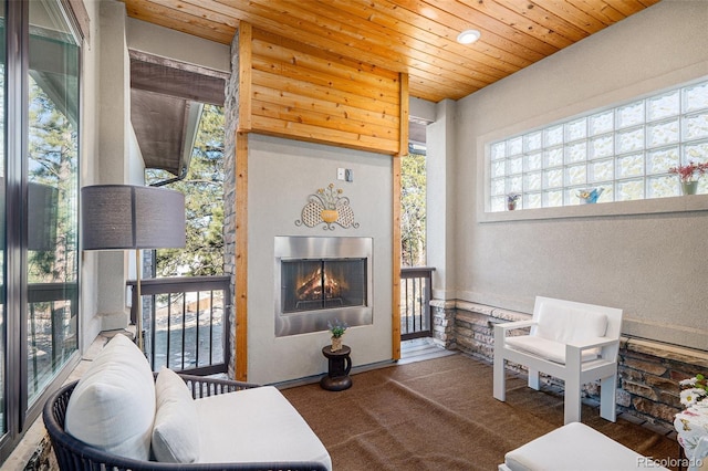 sitting room featuring wood ceiling, a warm lit fireplace, and carpet floors
