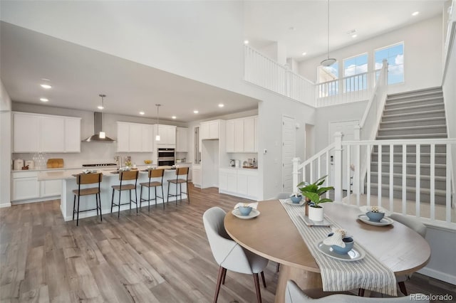 dining room featuring light wood finished floors, recessed lighting, stairs, and a high ceiling