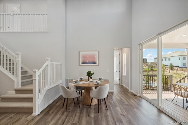 dining space featuring stairway, baseboards, a towering ceiling, and wood finished floors