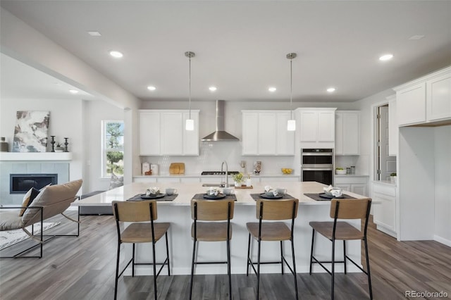 kitchen featuring backsplash, dark wood-style floors, double oven, a fireplace, and wall chimney range hood