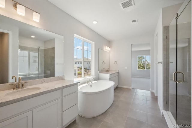 bathroom featuring visible vents, a shower stall, a freestanding bath, two vanities, and a sink