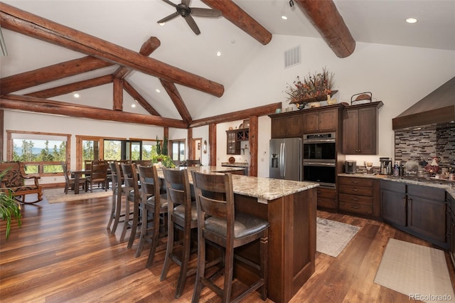 kitchen with a large island with sink, a breakfast bar area, light stone countertops, dark hardwood / wood-style flooring, and stainless steel appliances