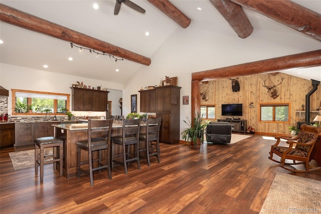 kitchen with high vaulted ceiling, dark hardwood / wood-style floors, wood walls, a kitchen bar, and a kitchen island