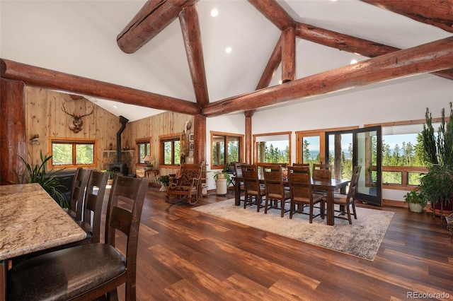 dining area with a wood stove, a healthy amount of sunlight, high vaulted ceiling, and dark wood-type flooring