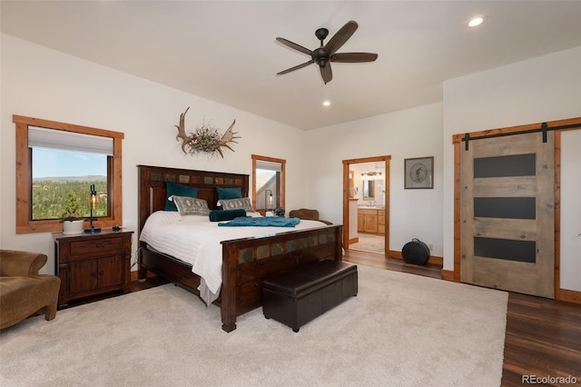 bedroom with a barn door, ensuite bathroom, ceiling fan, and hardwood / wood-style flooring