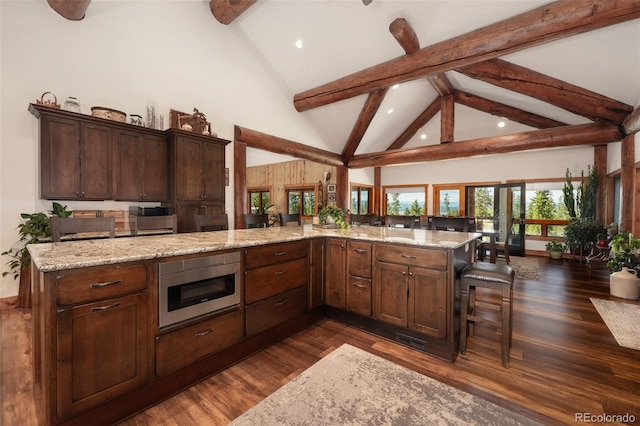 kitchen with light stone counters, dark hardwood / wood-style flooring, built in microwave, and a breakfast bar area