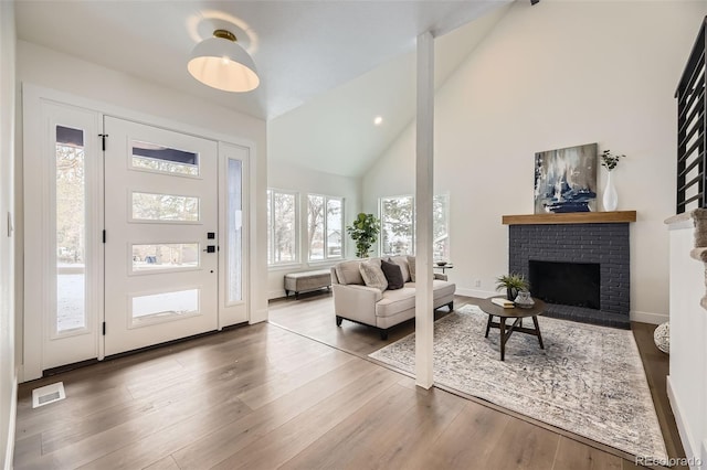 foyer with wood-type flooring, a brick fireplace, and high vaulted ceiling