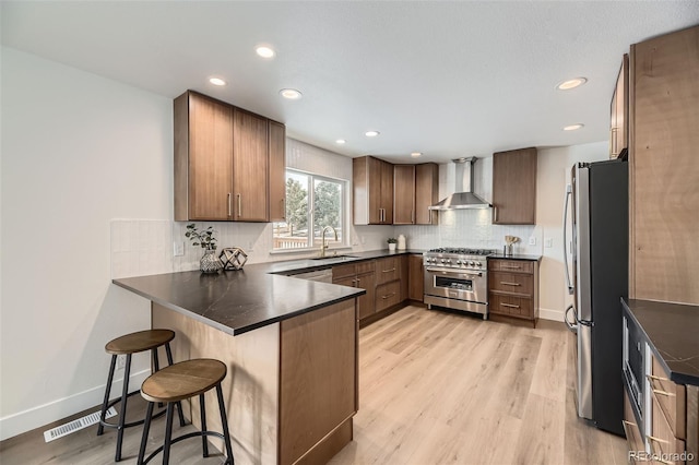 kitchen with sink, a kitchen breakfast bar, kitchen peninsula, stainless steel appliances, and wall chimney exhaust hood