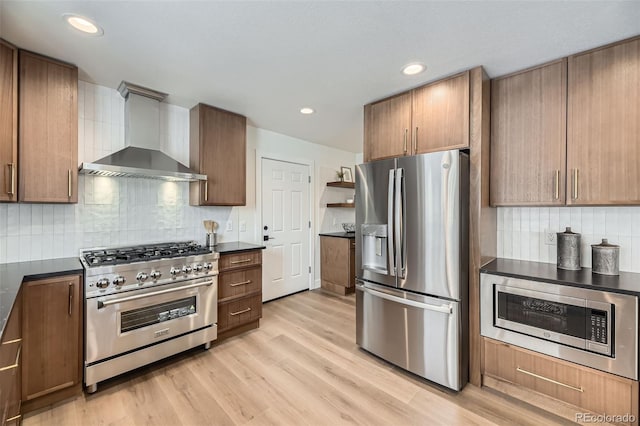 kitchen with stainless steel appliances, light wood-type flooring, decorative backsplash, and wall chimney range hood