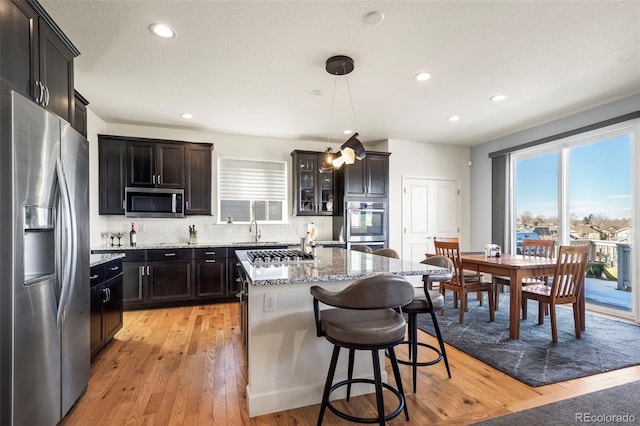 kitchen featuring light stone countertops, stainless steel appliances, pendant lighting, light hardwood / wood-style floors, and a kitchen island